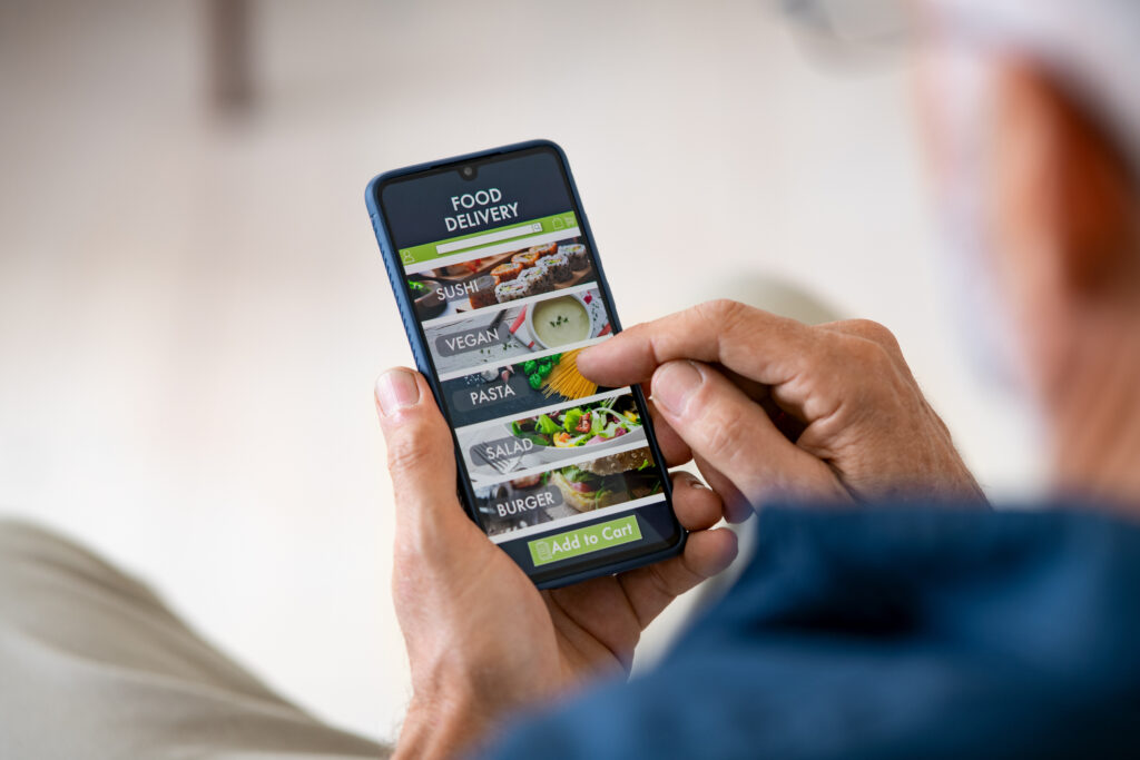Top view of man hands holding smartphone while order food delivery at home. Back view of mature man using food delivery app with mobile phone to order lunch.