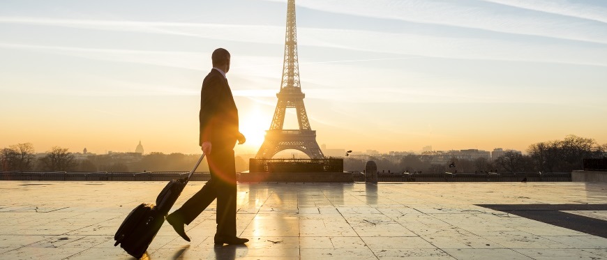 Man with suitcase walking past Eiffel Tower